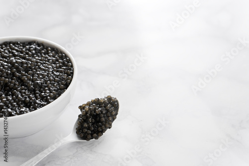 black caviar in bowl and on white shoop on marble background