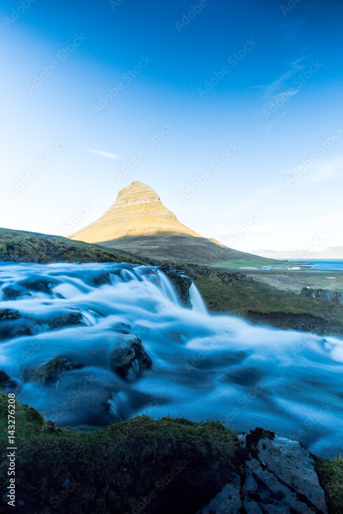 A waterfall called Kirkjufellfoss, that flows into the sea on western coast of Iceland. Next to the waterfall, is a free standing mountain called Kirkjufell located at the Snaefellsnes peninsula.