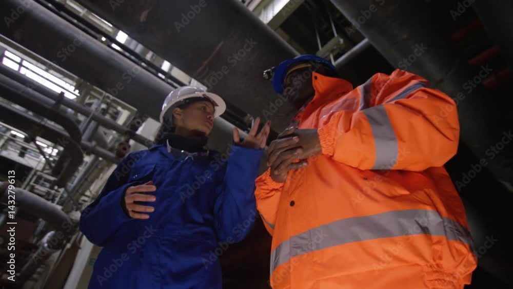 Low angle view male & female engineers in power station discussing operations Low angle view male & female engineers in power station discussing operations