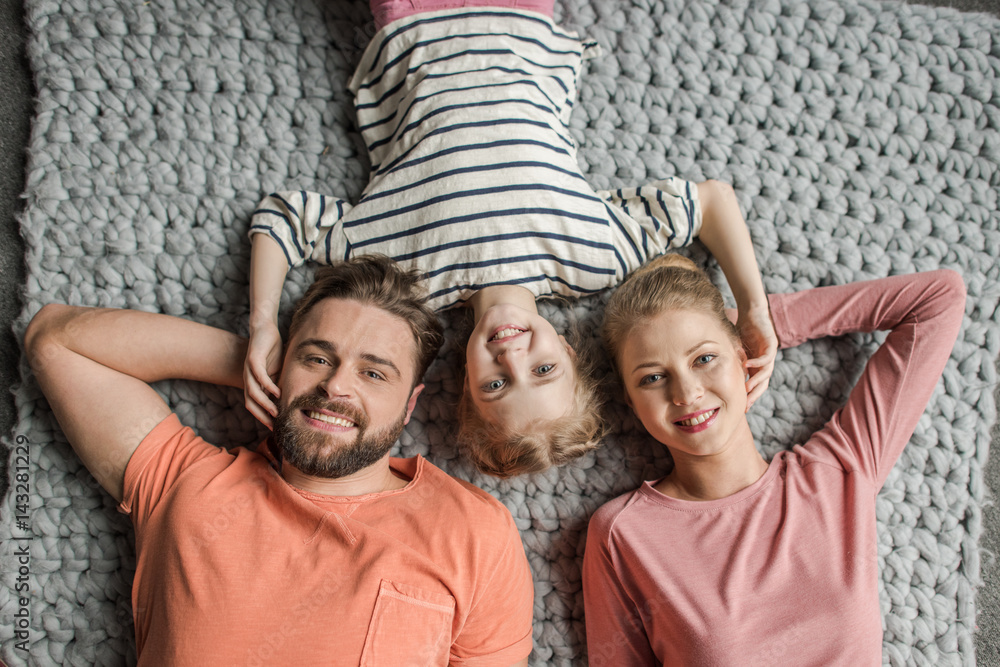 Top view of happy family with one child lying together on grey knitted carpet