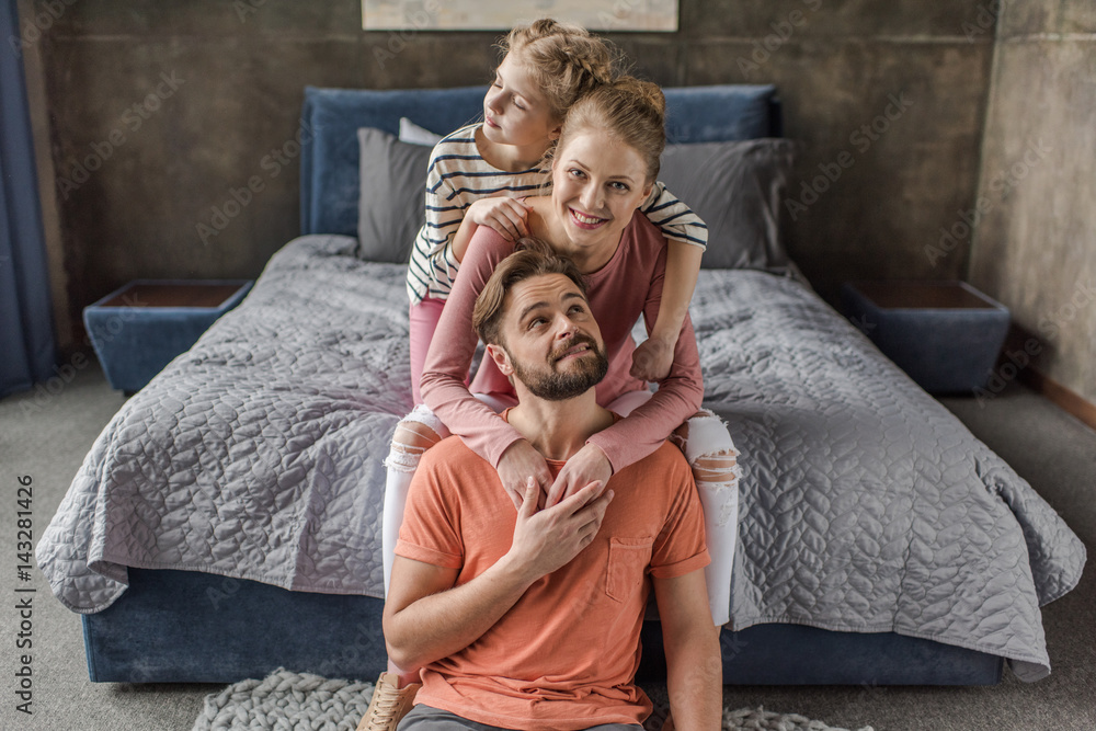 Happy young family with one child sitting together and hugging in bedroom