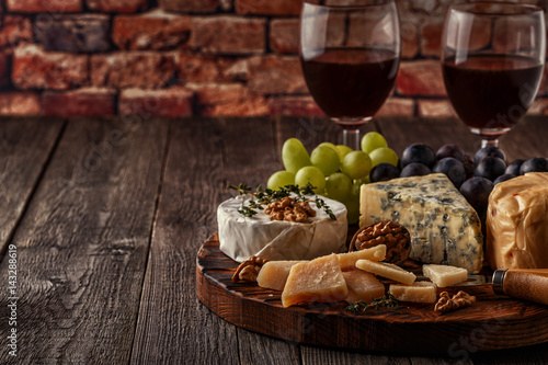 Cheese, nuts, grapes and red wine on wooden background.