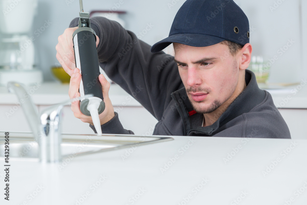 young handyman applying silicone sealant with gun around sink young handyman applying silicone sealant with gun around sink