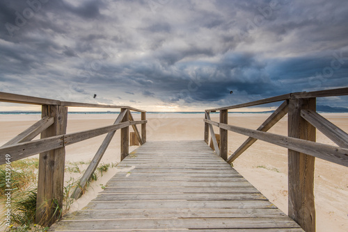 wooden bridge on beach with dark clouds before storm