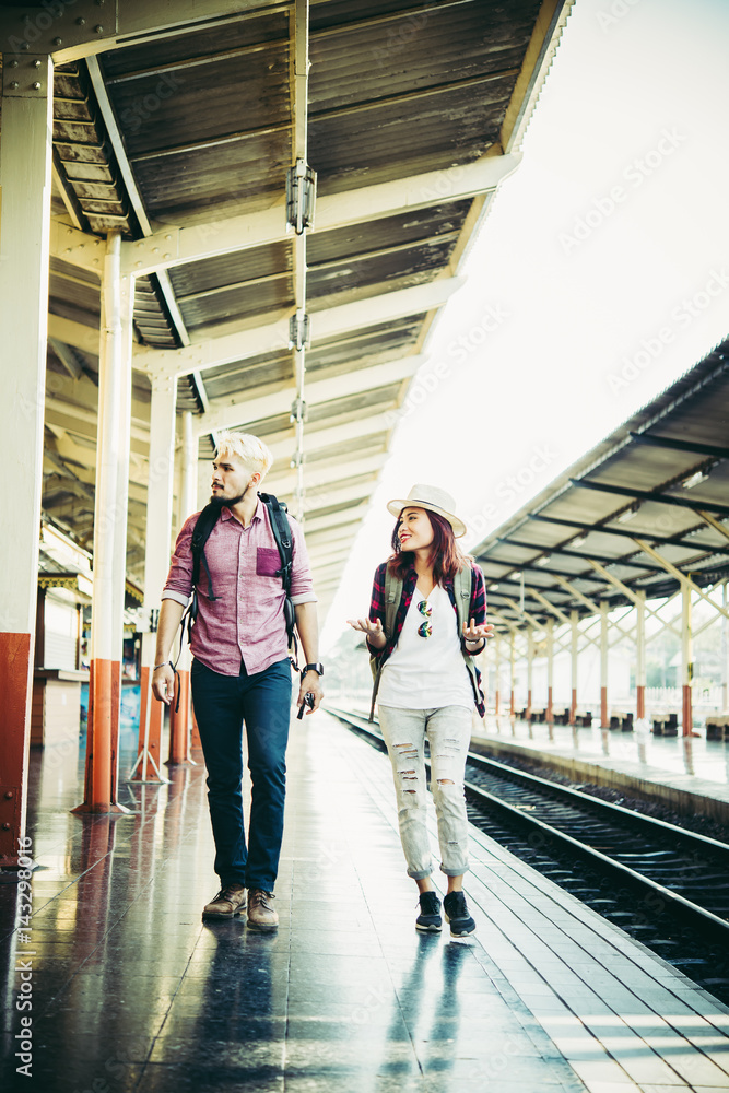 Hipster couple walking on platform at the train station. Two young tourist are ready to get on the train and begin their journey. Travel concept.