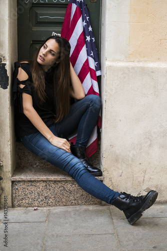 Portrait of young woman sitting at house entrance with US American flag
