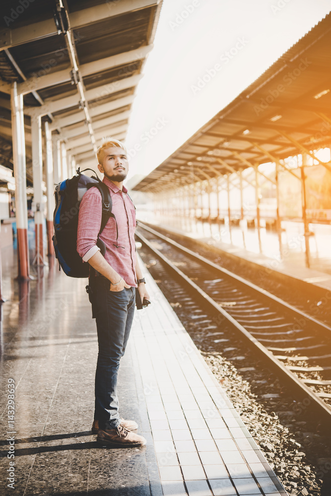 Young tourist man with backpack standing on platform waiting for train at train station, vintage tone filter effects.Travel concept. Young tourist man with backpack standing on platform waiting for train at train station, vintage tone filter effects.Travel concept.