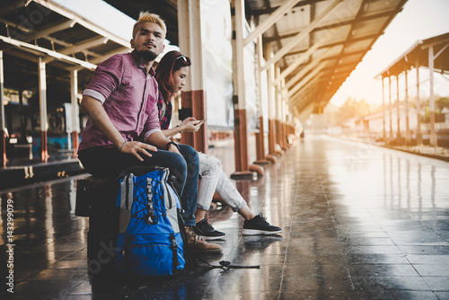 Young tourist couple with backpack sitting on bench at the train station. Two young tourist are waiting to get on the train and begin their journey. Travel concept. © MollyP