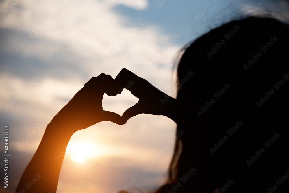 Silhouette hand making heart with sunset