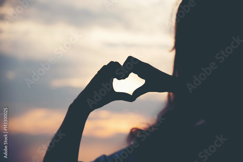 Silhouette hand making heart with sunset