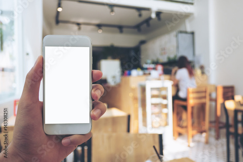 Mockup image of hand holding mobile phone with blank white screen in wooden cafe