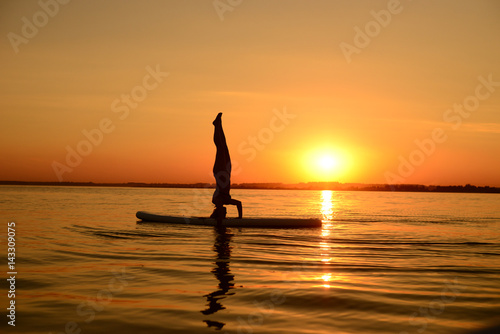 Beautiful young sporty woman is training upside down on the surf desk at sunset time