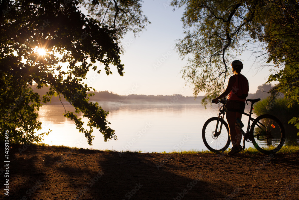 Fototapeta premium Woman riding bicycle on the sunset in the park.