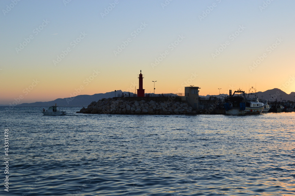 Paisaje marinero ,faro y barca en una puesta de sol en el puerto de Cambrils,Cataluña,Spain.