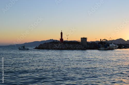 Paisaje marinero ,faro y barca en una puesta de sol en el puerto de Cambrils,Cataluña,Spain.