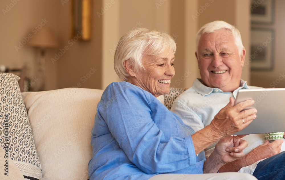Smiling seniors browsing the internet from their living room sofa Smiling seniors browsing the internet from their living room sofa