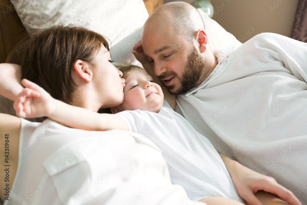 beautiful mother and handsome father with baby daughter lying on bedroom beautiful mother and handsome father with baby daughter lying on bedroom