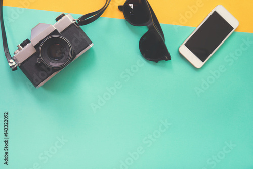 Flat lay design of work desk with sunglasses old camera and smartphone on green and yellow background.