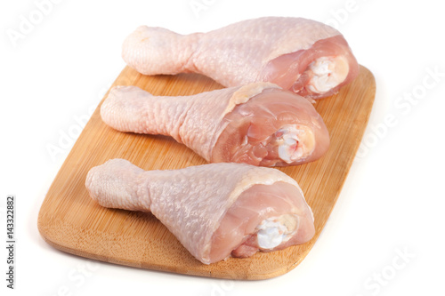 three raw chicken drumsticks on a wooden cutting boardn isolated on white background photo