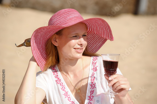Blonde in a chaise longue on the beach wearing a hat with a glass of wine photo