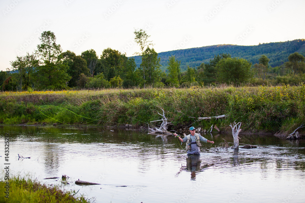 Senior flyfishing in a river at sunset