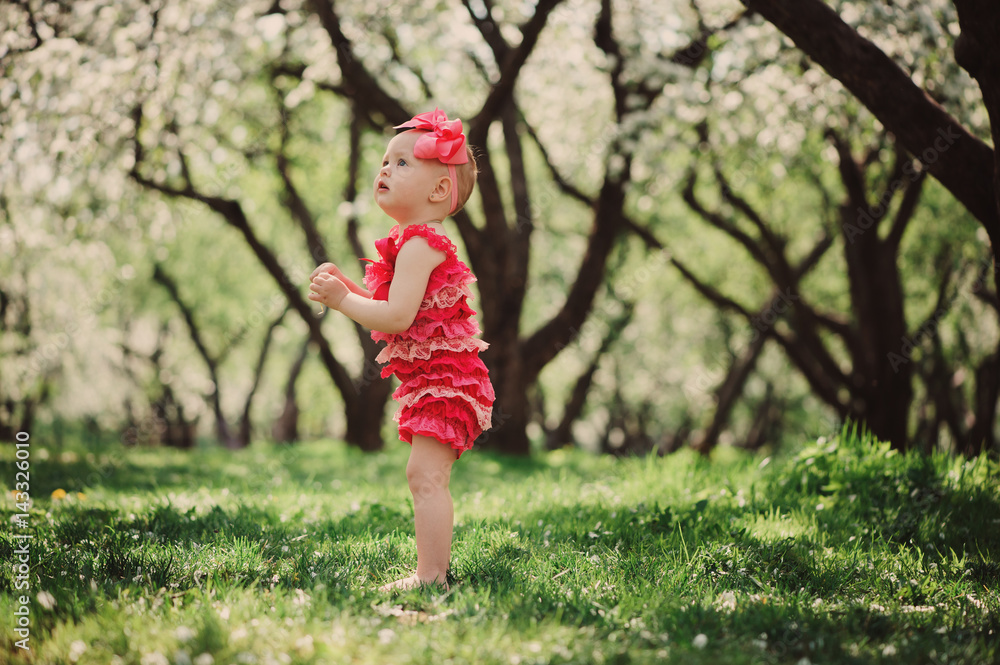 cute happy baby girl in funny pink romper walking outdoor in spring garden. Happy childhood concept cute happy baby girl in funny pink romper walking outdoor in spring garden. Happy childhood concept