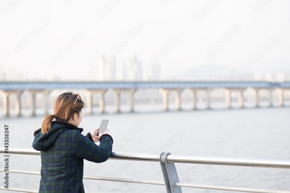 Woman waer fleece jacket standing and looking at smartphone in chilling day in evening at river side. Feeling lonely or chilling. Woman waer fleece jacket standing and looking at smartphone in chilling day in evening at river side. Feeling lonely or chilling.