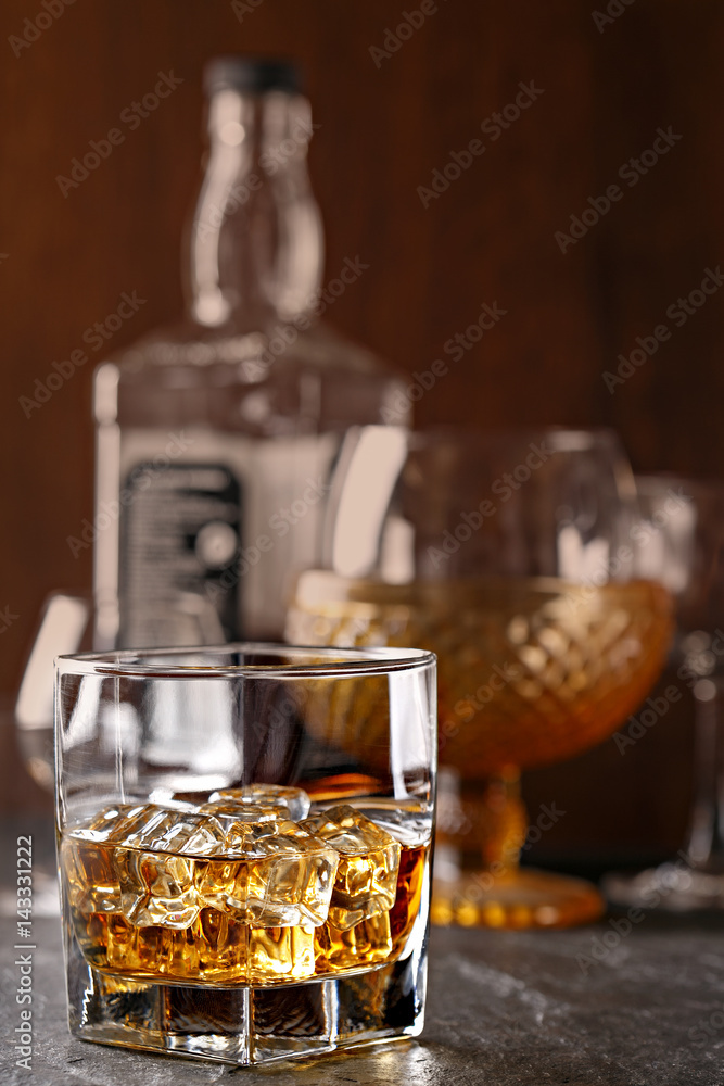 Whiskey glass close-up. Cold with ice, bottle in the background Whiskey glass close-up. Cold with ice, bottle in the background