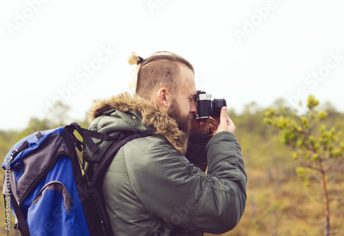 Handsome, bearded guy hiking in swamps and taking pictures of autumn forest. Camp, adventure, trip, concept.