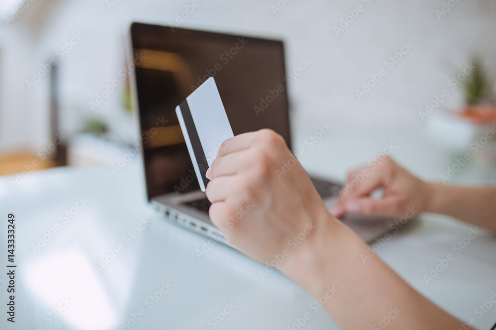 Close up and part of human hand using laptop and holding credit card indoors alone Close up and part of human hand using laptop and holding credit card indoors alone