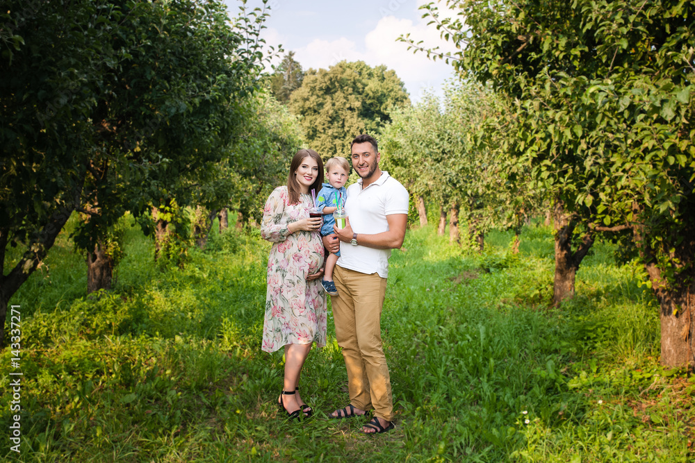 Young attractive family playing with child in a meadow and drinking juice Young attractive family playing with child in a meadow and drinking juice