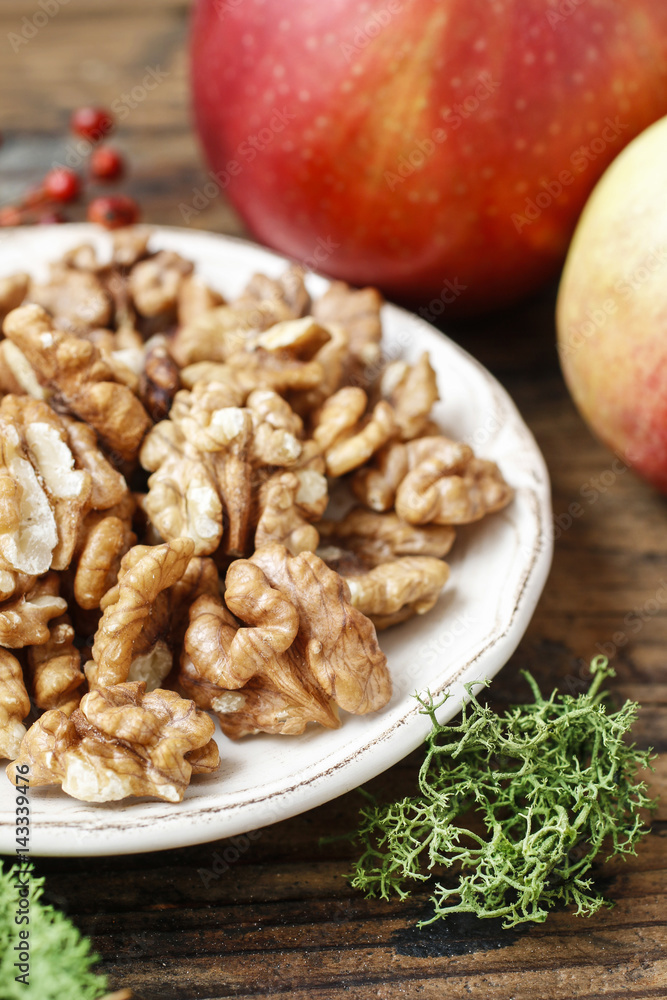 Fototapeta premium Bowl of walnuts and red apples on wooden table