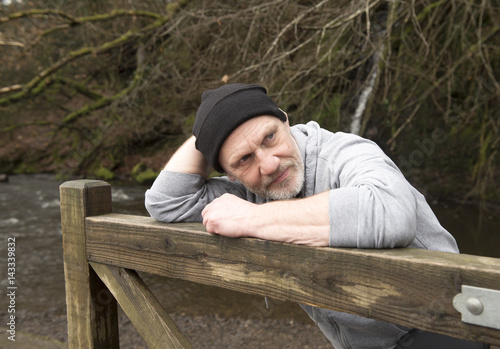 Casual mature man leaning against an old wooden gate outdoors 