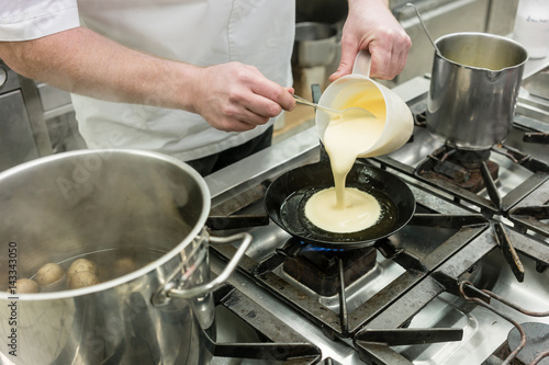 Chef preparing pancake dessert pouring dough into pan in kitchen