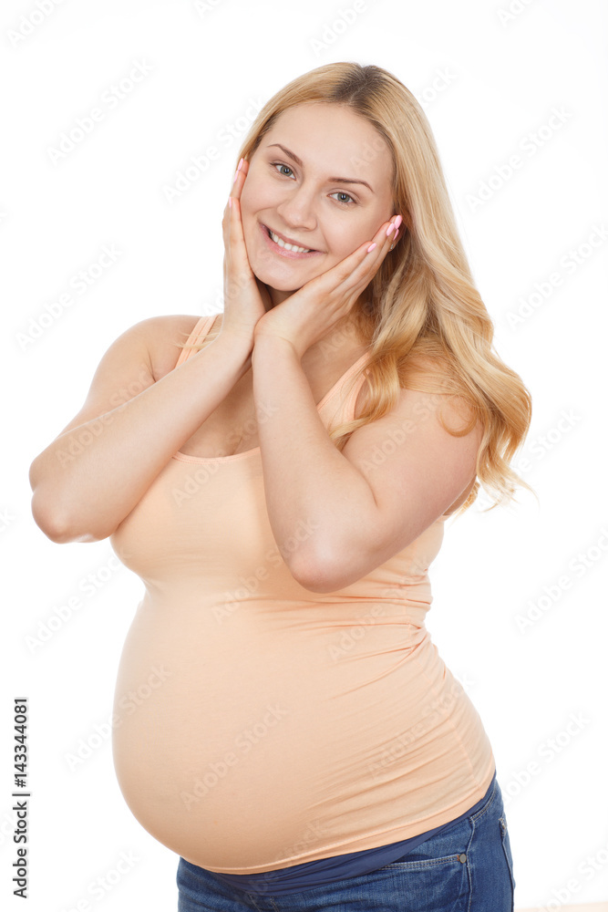 Joy of becoming a mother. Vertical portrait of a beautiful pregnant woman posing at the studio looking to the camera smiling touching her face isolated on white.