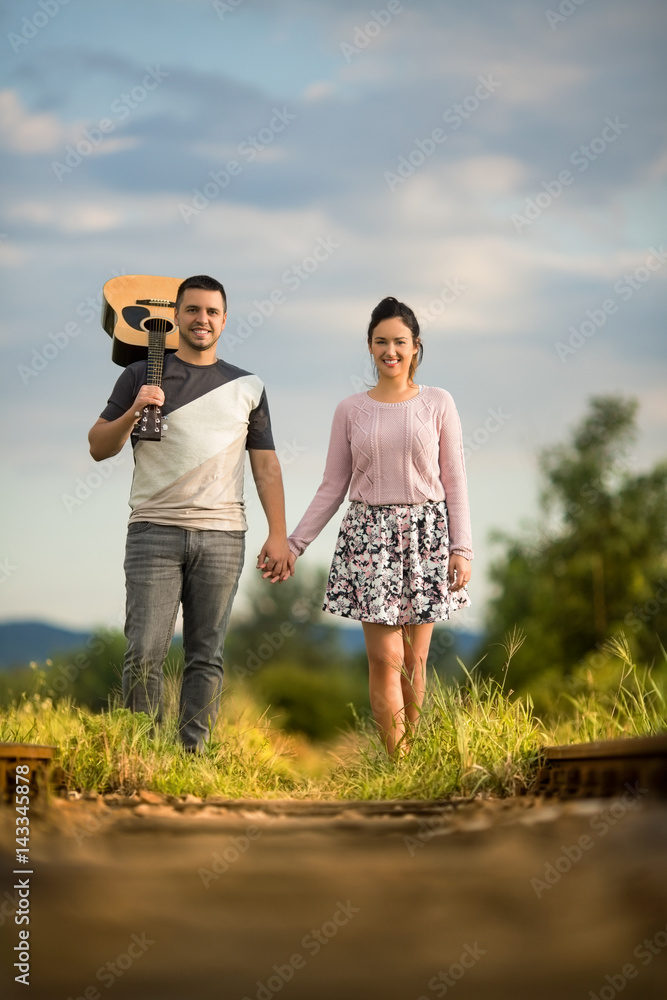 Beautiful couple walking on a ralroad track and holding hands