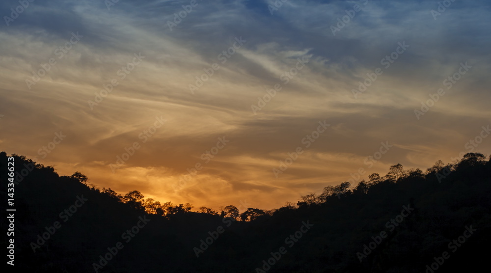 Mountain forest landscape under evening sky with clouds in sunlight and trees silhouettes. Majestic sunset in indian Himalaya mountains near Rishikesh, Uttharakand.