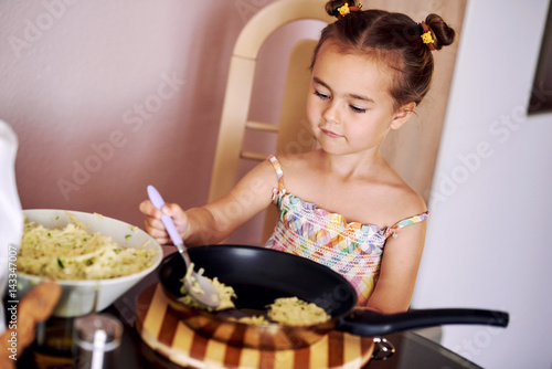Cute little girl cooking potato pancakes at home photo
