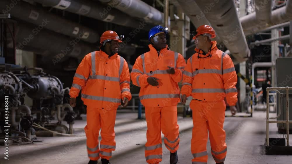 Engineers walking through power plant with other workers in background Engineers walking through power plant with other workers in background