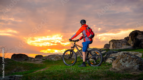 Cyclist with his Mountain Bike Looking at the Beautiful Sunset on Spring Rocky Trail. Extreme Sports and Adventure Concept.