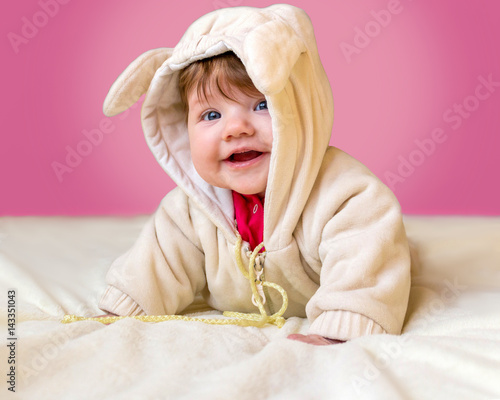 Little beautiful baby in a funny costume with ears laughs, lying on his stomach. photo