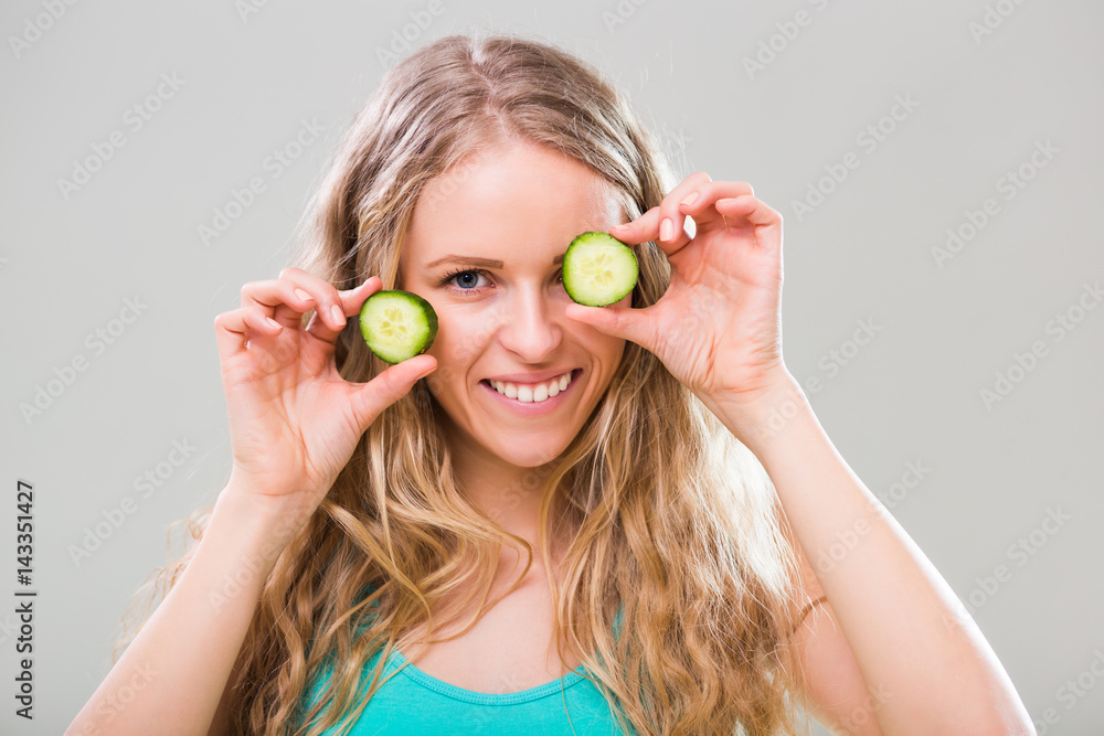 Beautiful young woman showing slices of cucumber on gray background. Beautiful young woman showing slices of cucumber on gray background.