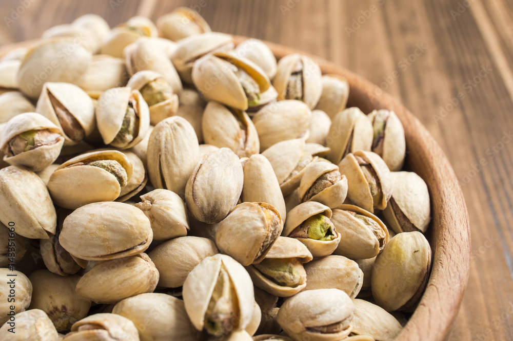 parted ripe pistachio nuts in a bowl on a wooden table parted ripe pistachio nuts in a bowl on a wooden table