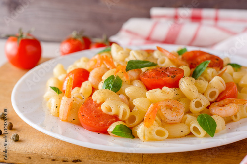 Pasta with shrimps, cherry tomatoes and basil in white plate.