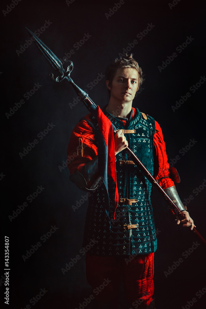 Young medieval warrior with the spear. Dark background. Young medieval warrior with the spear. Dark background.