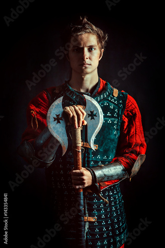 Young medieval warrior with the axe. Dark background. photo