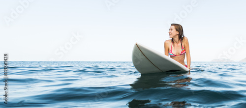Photography Young woman sits on the surfboard in the ocean and waiting a wave