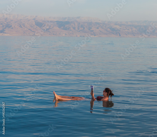 KALIA BEACH, ISRAEL - FEBRUARY 27, 2017: Young woman reads a book floating in the waters of the Dead Sea in Israel