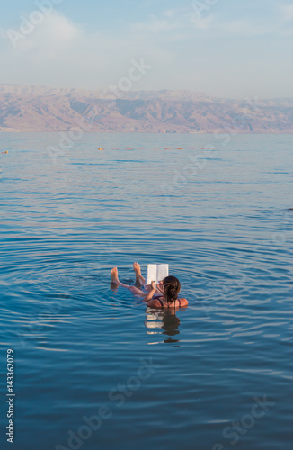 Foto Young woman reads a book floating in the waters of the Dead Sea in Israel
