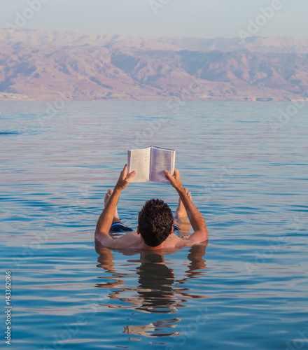 Tableau sur toile Young man reads a book floating in the waters of the Dead Sea in Israel